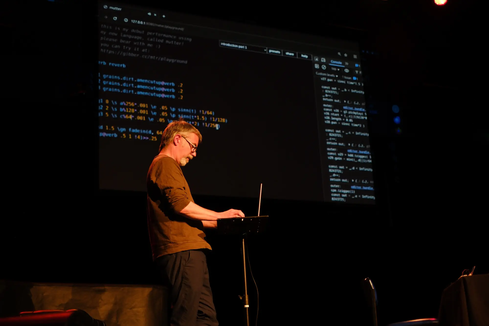 Me in front of a large screen projecting code from a performance, live coding on a laptop.